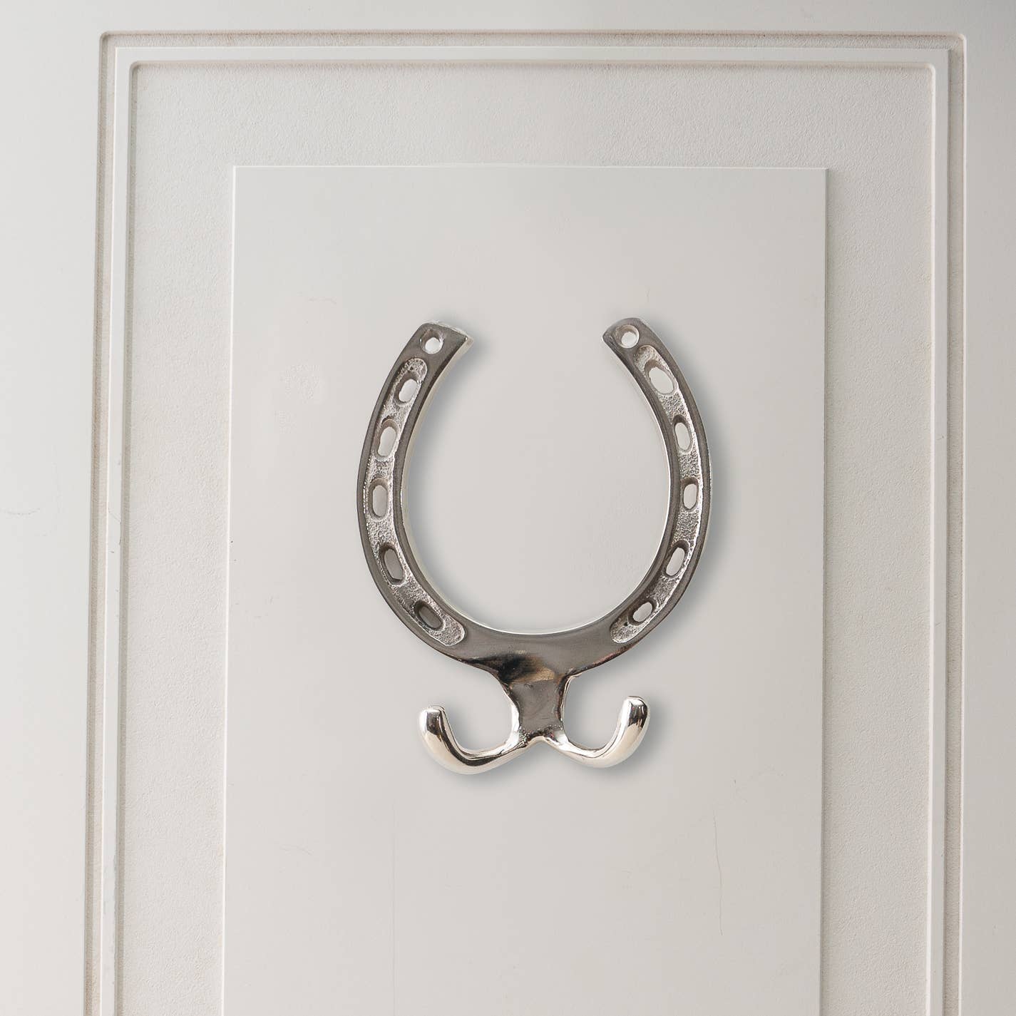 A nickel horseshoe-shaped wall hook with a silver finish mounted on a white wall.