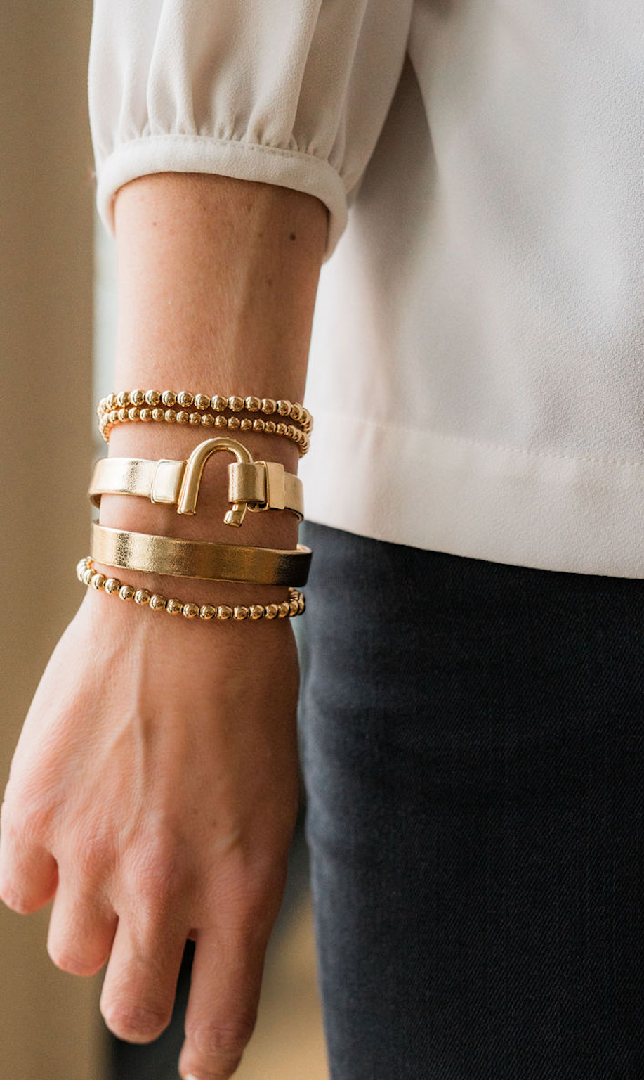 A person's wrist wearing a gold-colored horseshoe metallic leather bracelet wrap with a white sleeve of a shirt.