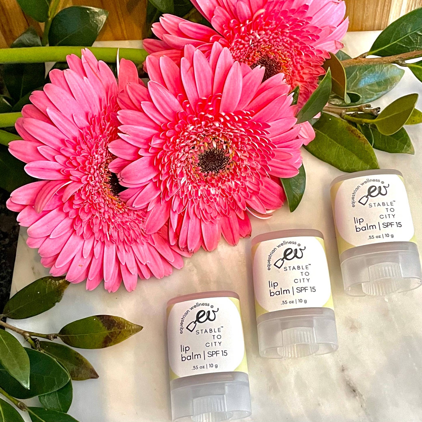 three sticks of organic lip balm on a marble coutnertop with a boquet of flowers