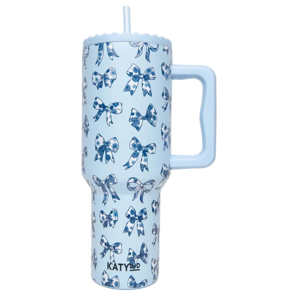 A person holding a blue tumbler with a floral pattern of blue ribbons and bows, featuring a reusable plastic straw and an adjustable straw cover.