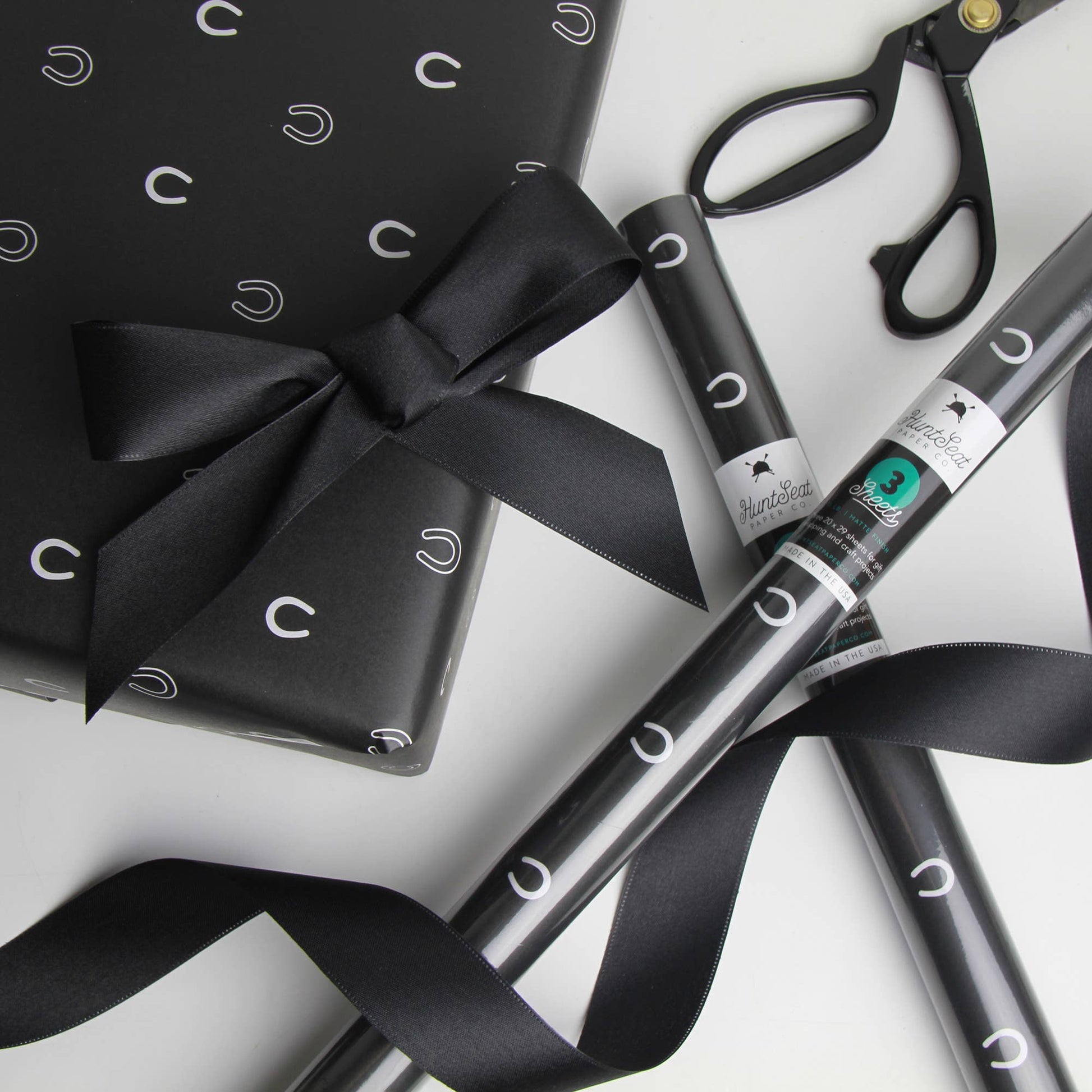 Black horse shoe gift wrap with a bow, black pen, and scissors on a white background