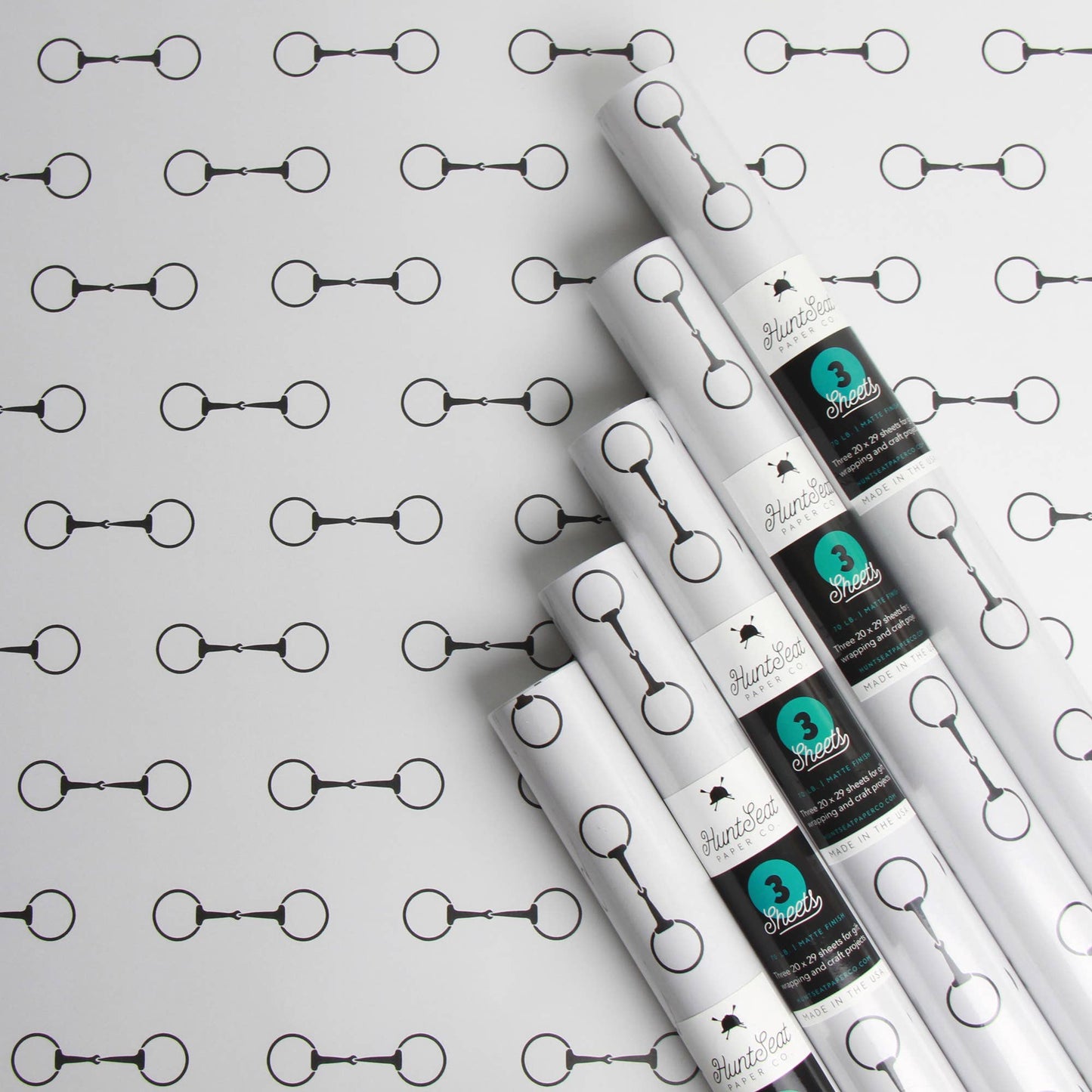 Rolls of white paper with black and teal labels on a horse bit patterned background