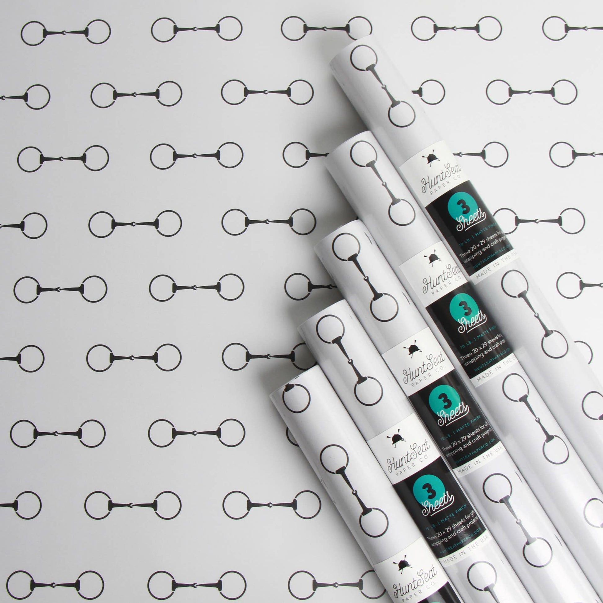Rolls of white paper with black and teal labels on a horse bit patterned background