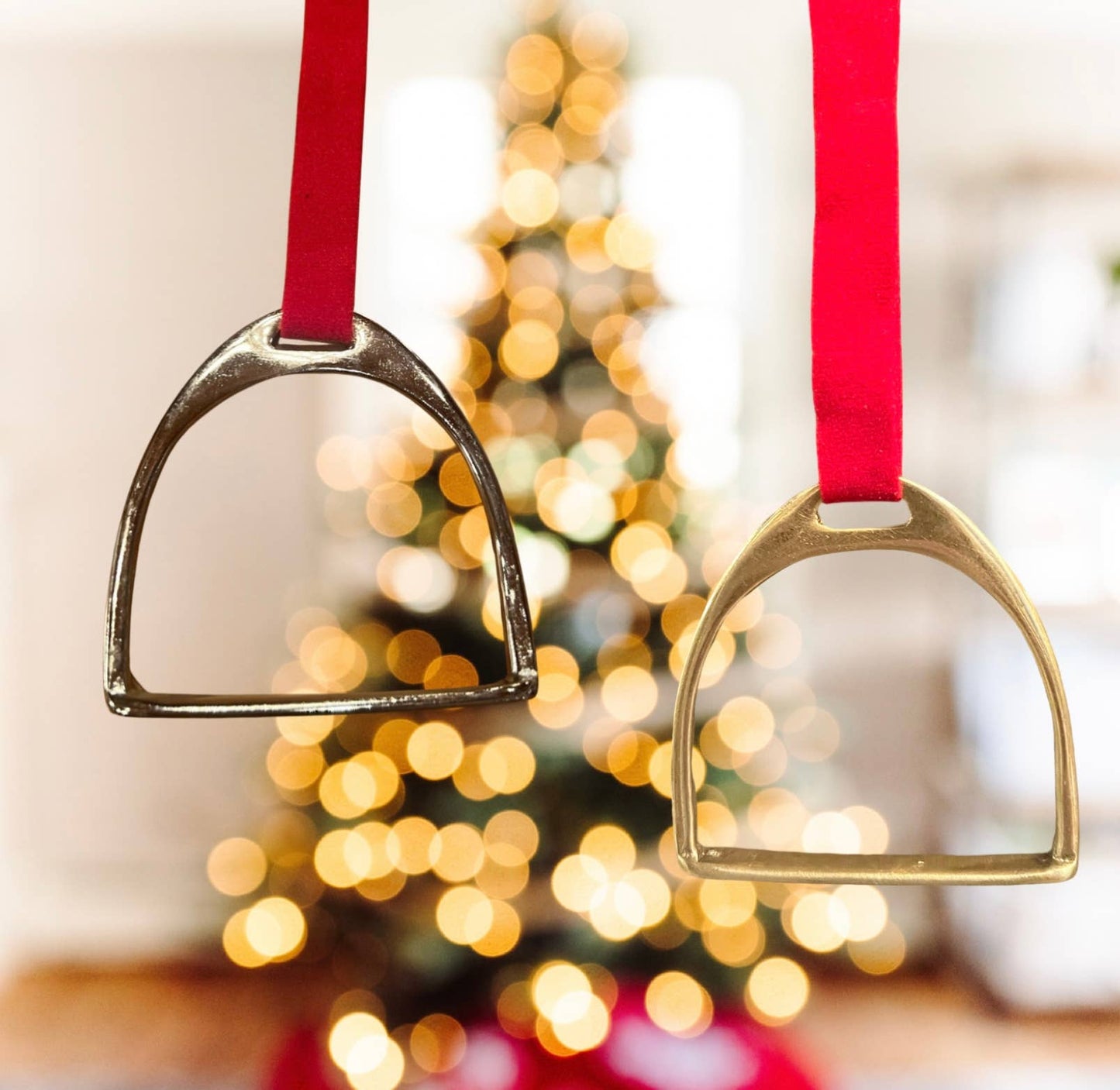 Two metal stirrups on red ribbons with a blurred Christmas tree in the background
