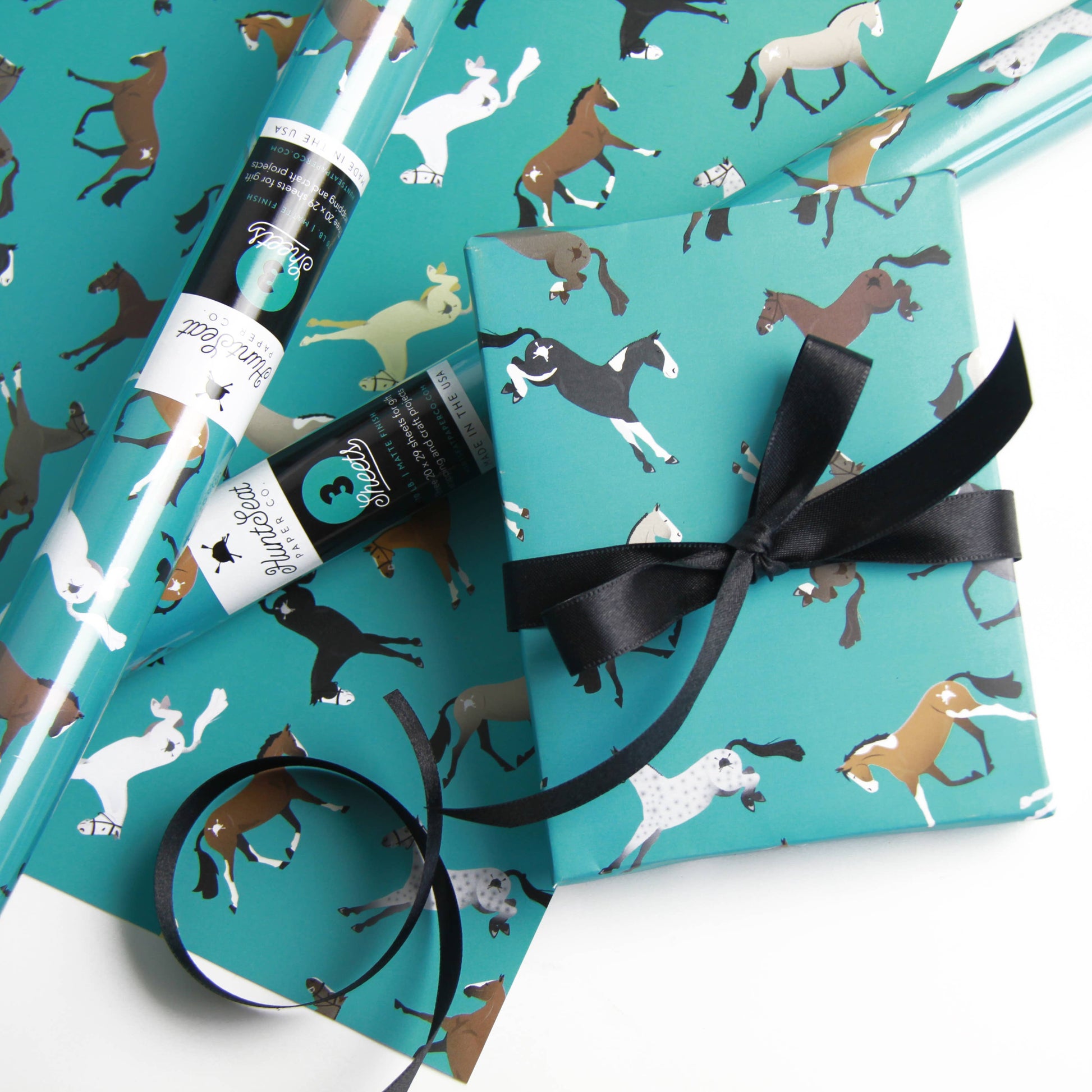 Turquoise wrapping paper with horse pattern and black ribbon on a white background