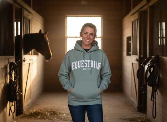 Woman wearing an 'Equestrian Athletics' hoodie in a stable with a horse. Perfect Equestrian gift