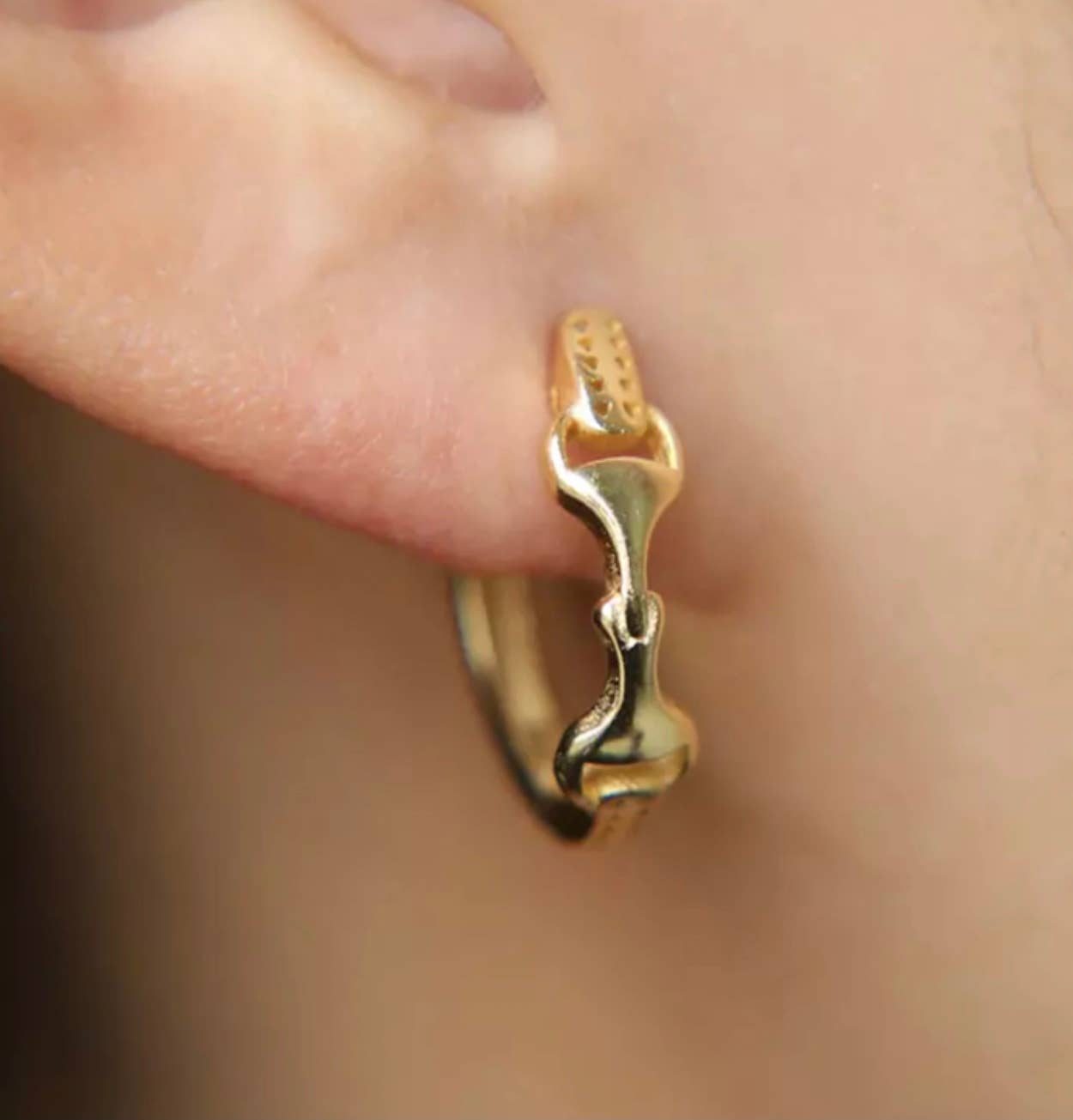 gold snaffle bit hoop earrings for equestrian displayed on a person's ear.