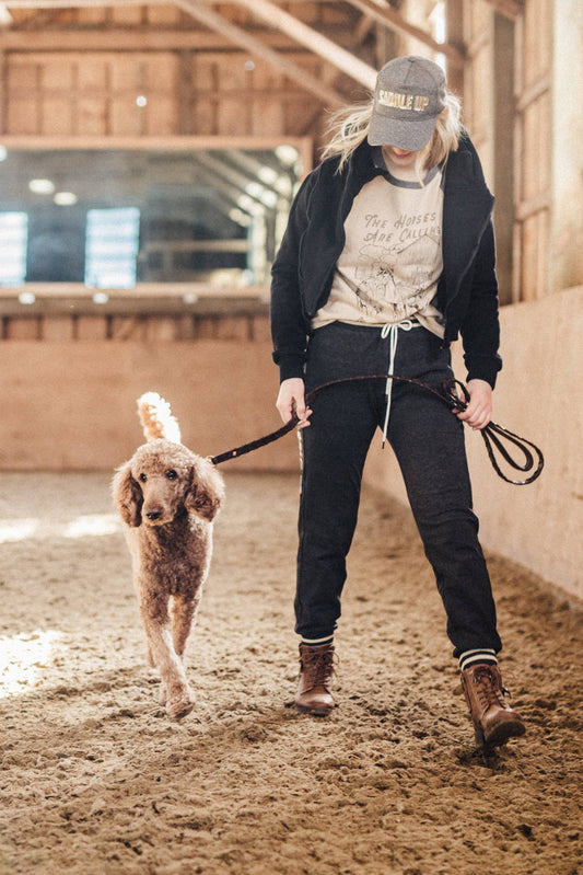 Gray jogger-style sweatpants featuring "Saddle Up" written in white lettering with a gold sparkle outline on a girl walking her dog in an equestrian setting