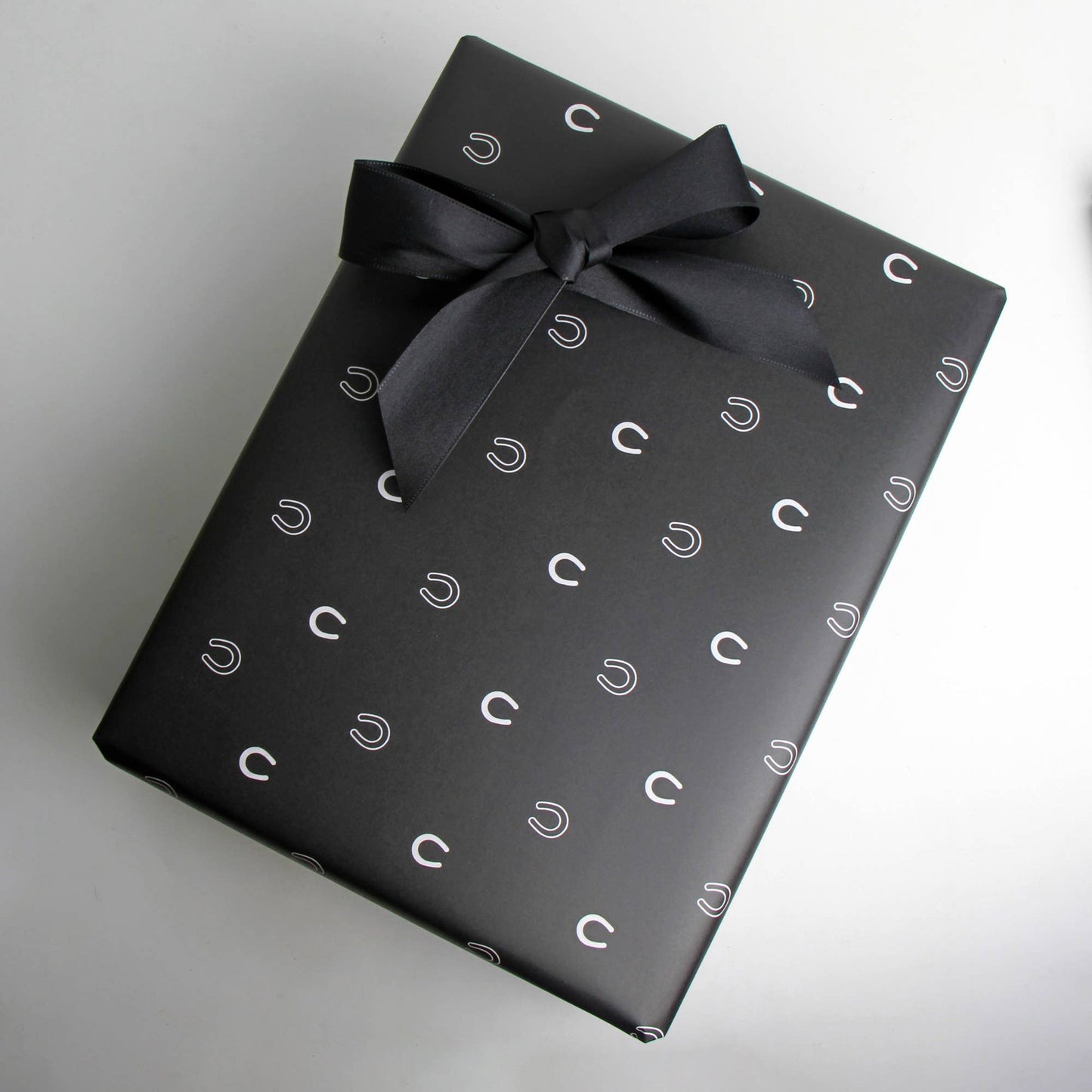Black gift wrap with white horse show patterns and a black bow on a light gray background