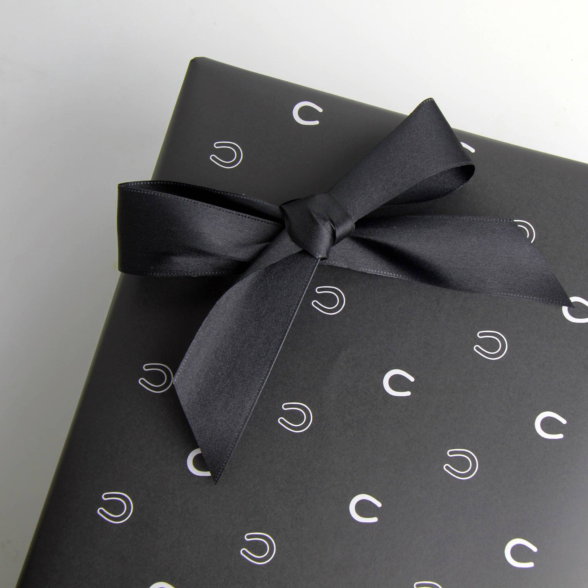 Black gift box with horse show design with a black ribbon on a light gray background