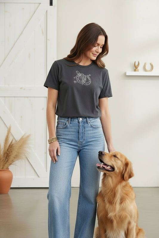 Gray t-shirt with a graphic horse shoe design on a model with her dog in a living room