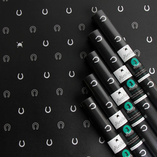 Black wrapping paper rolls with branded labels on a black background with horse shoe patterns. Wrapping paper for the holidays