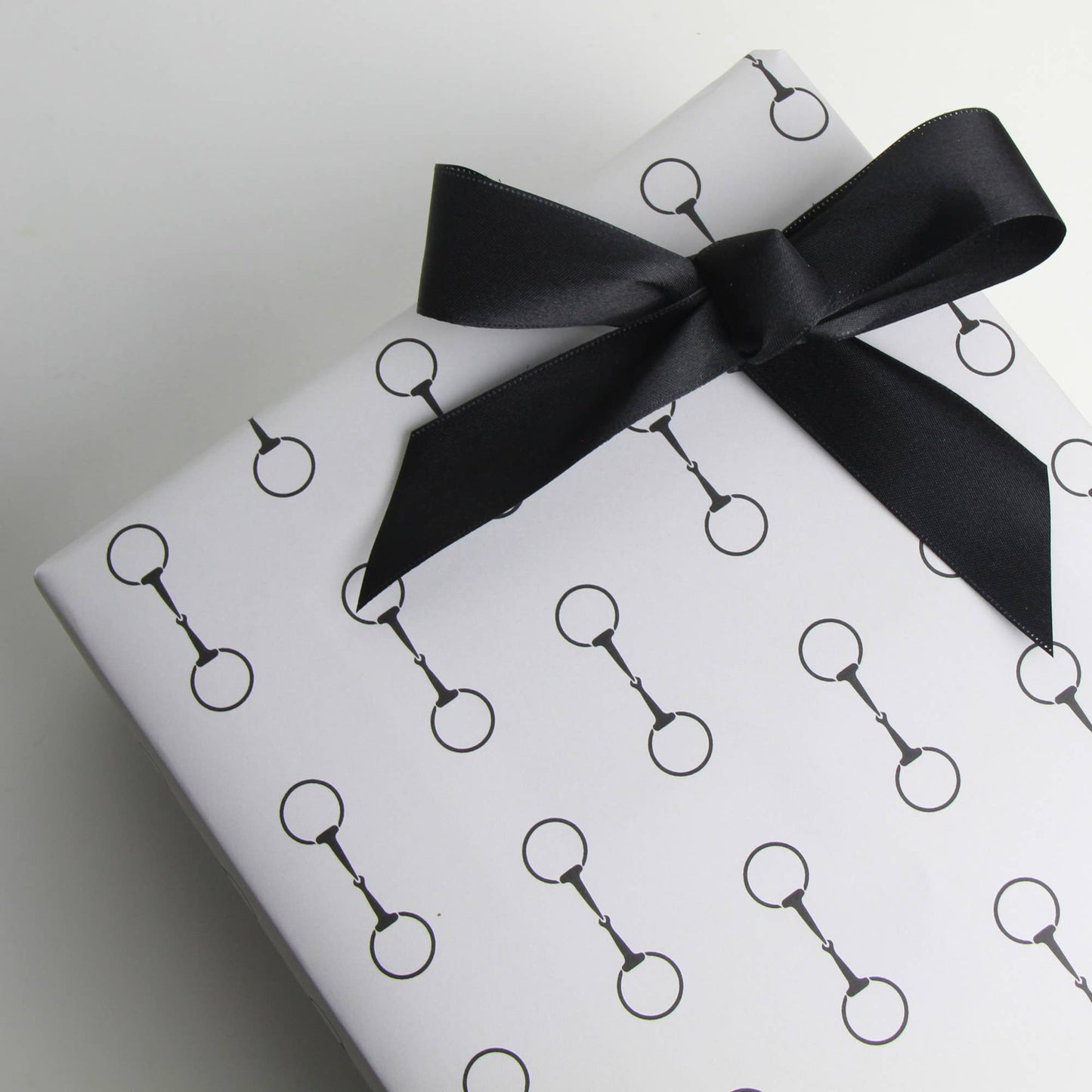 Gift wrapped in white paper with black snaffle bit pattern and black ribbon on a light gray background