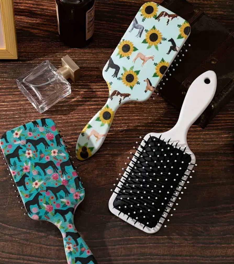 three paddle brushes, with horse and flower designs on a wooden vanity