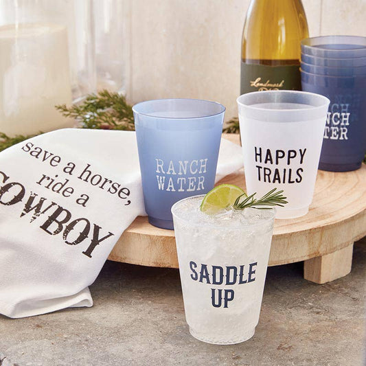 reuseable plastic cups, with cowboy sayings, on a cutting board with a dish towel and a bottle of wine