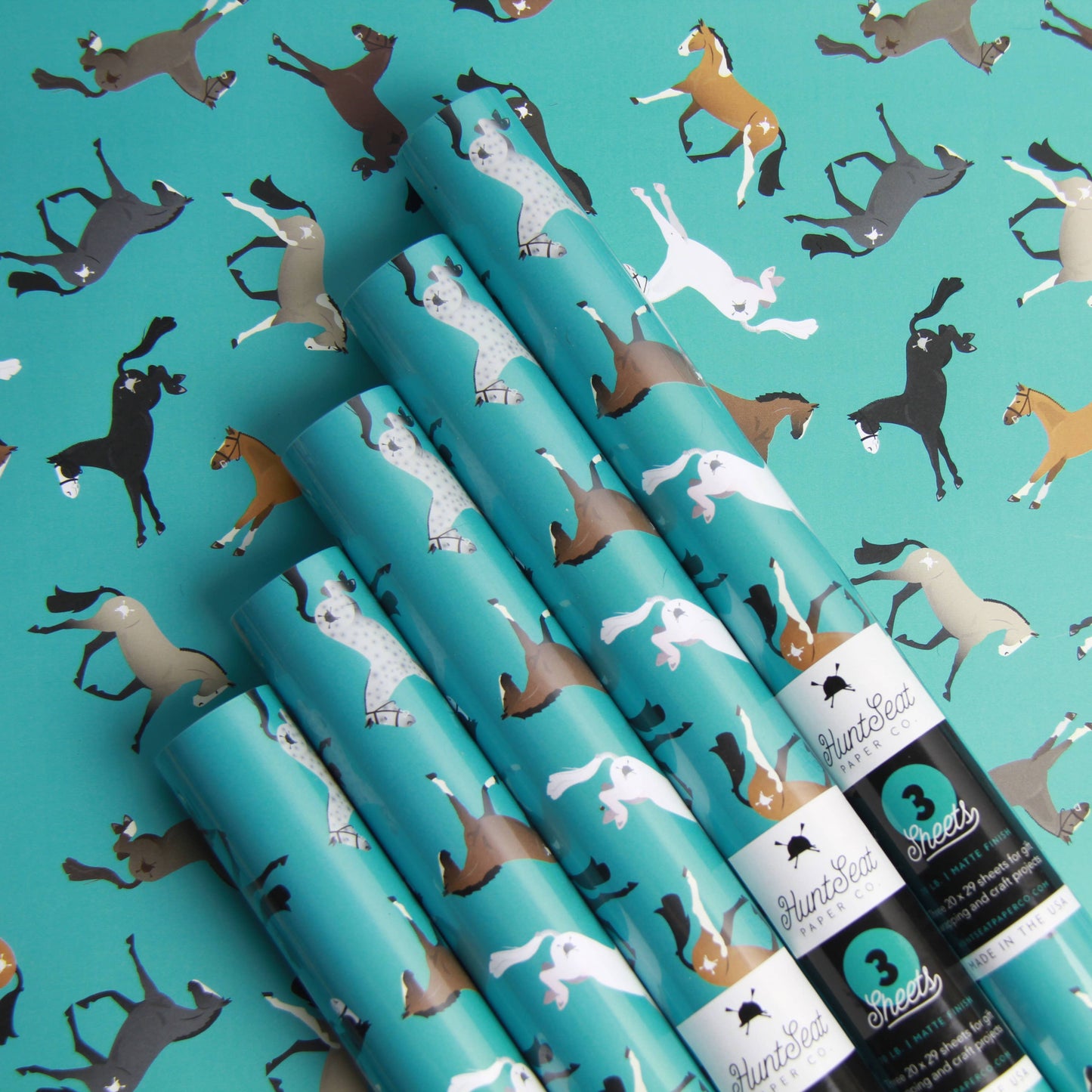 Rolls of teal wrapping paper with horse pattern on a teal background