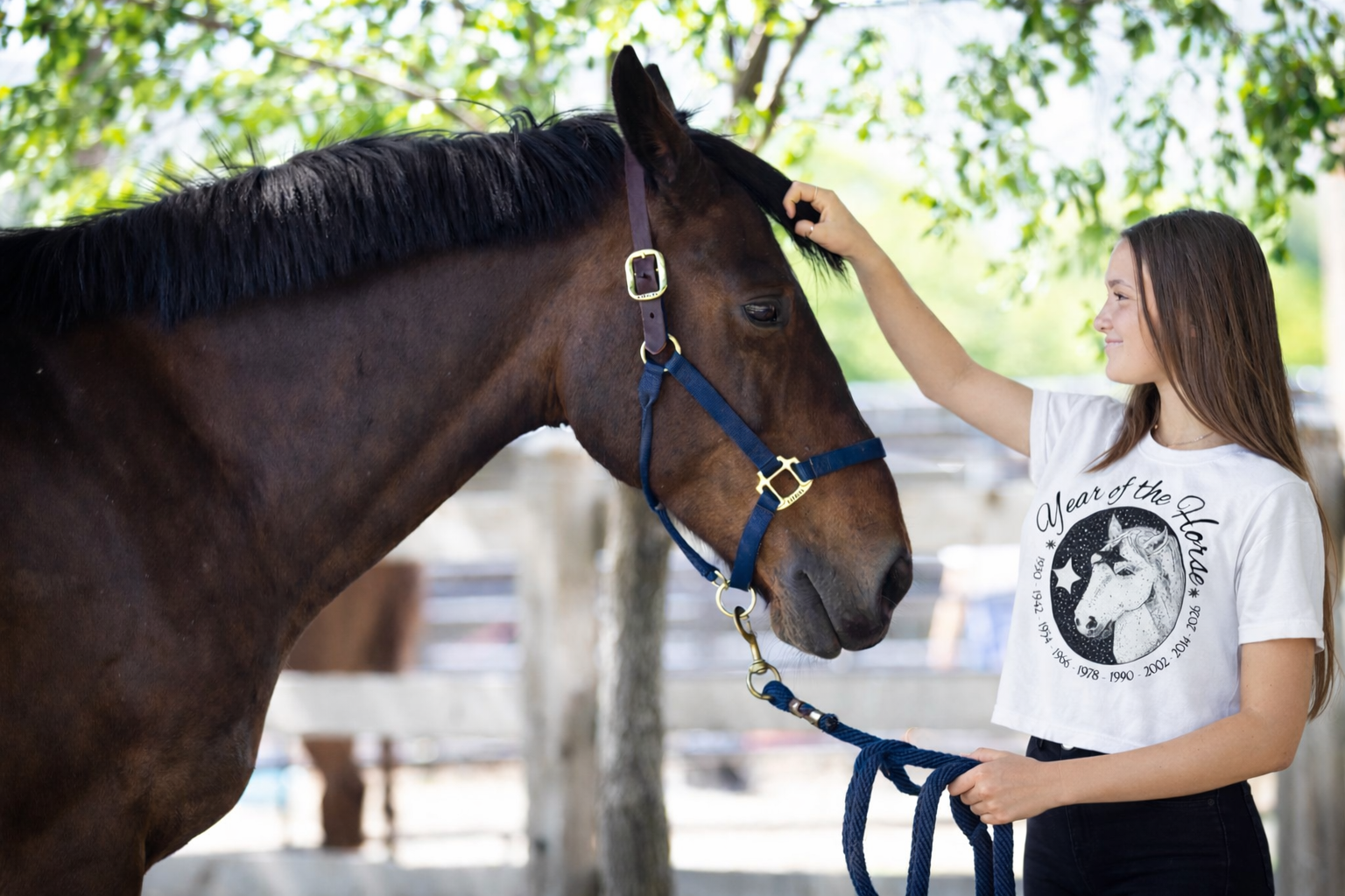 Woman petting a horse with a blurred background wearing a year of the horse white crewneck tee