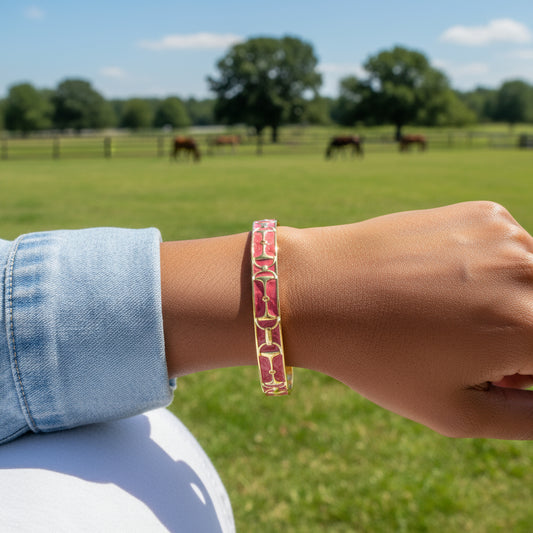 Gold and pink bracelet with 'Lauren Adams' branding  and a snaffle bit design on a farm background