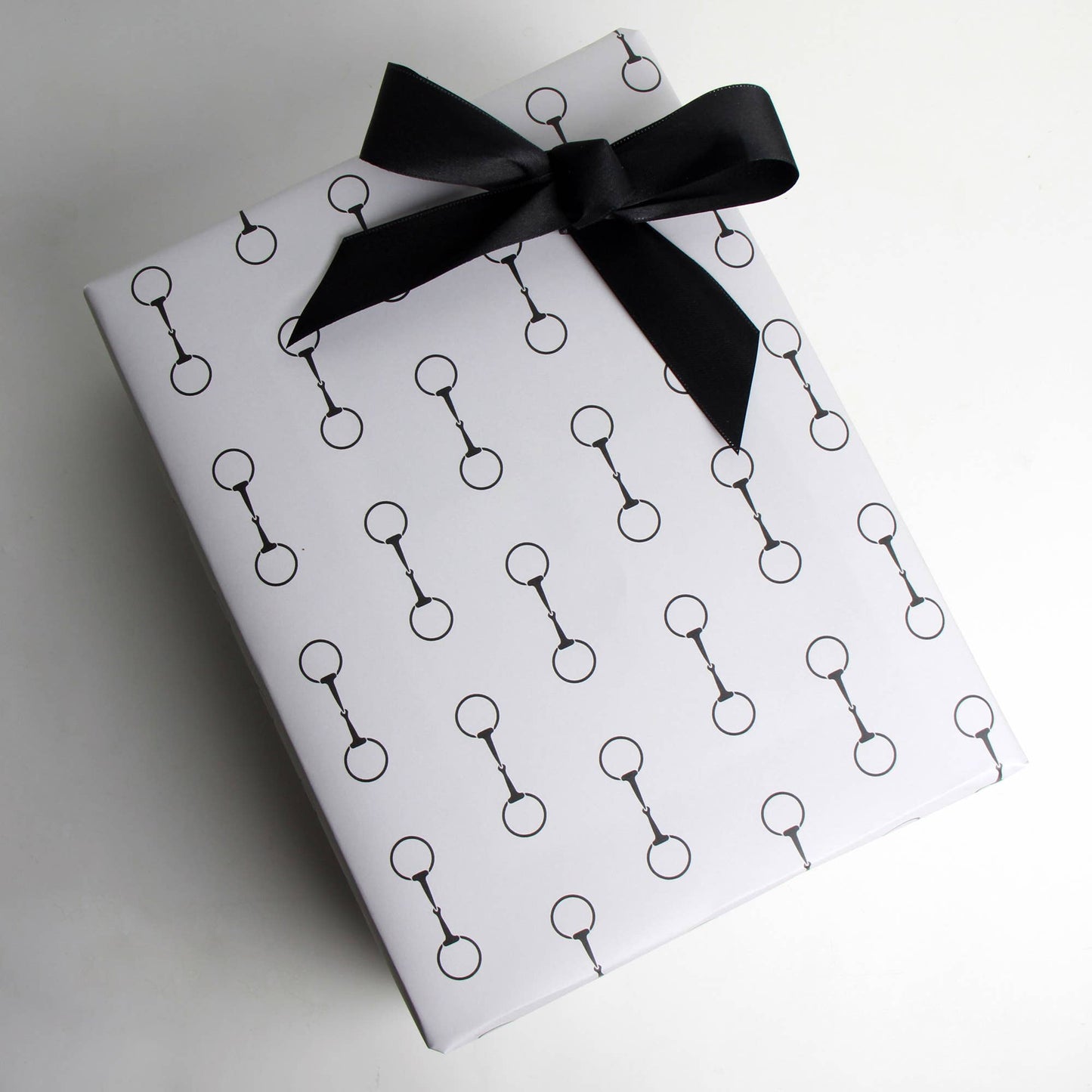 Gift box wrapped in paper with black snaffle bit pattern and tied with a black ribbon on a white background