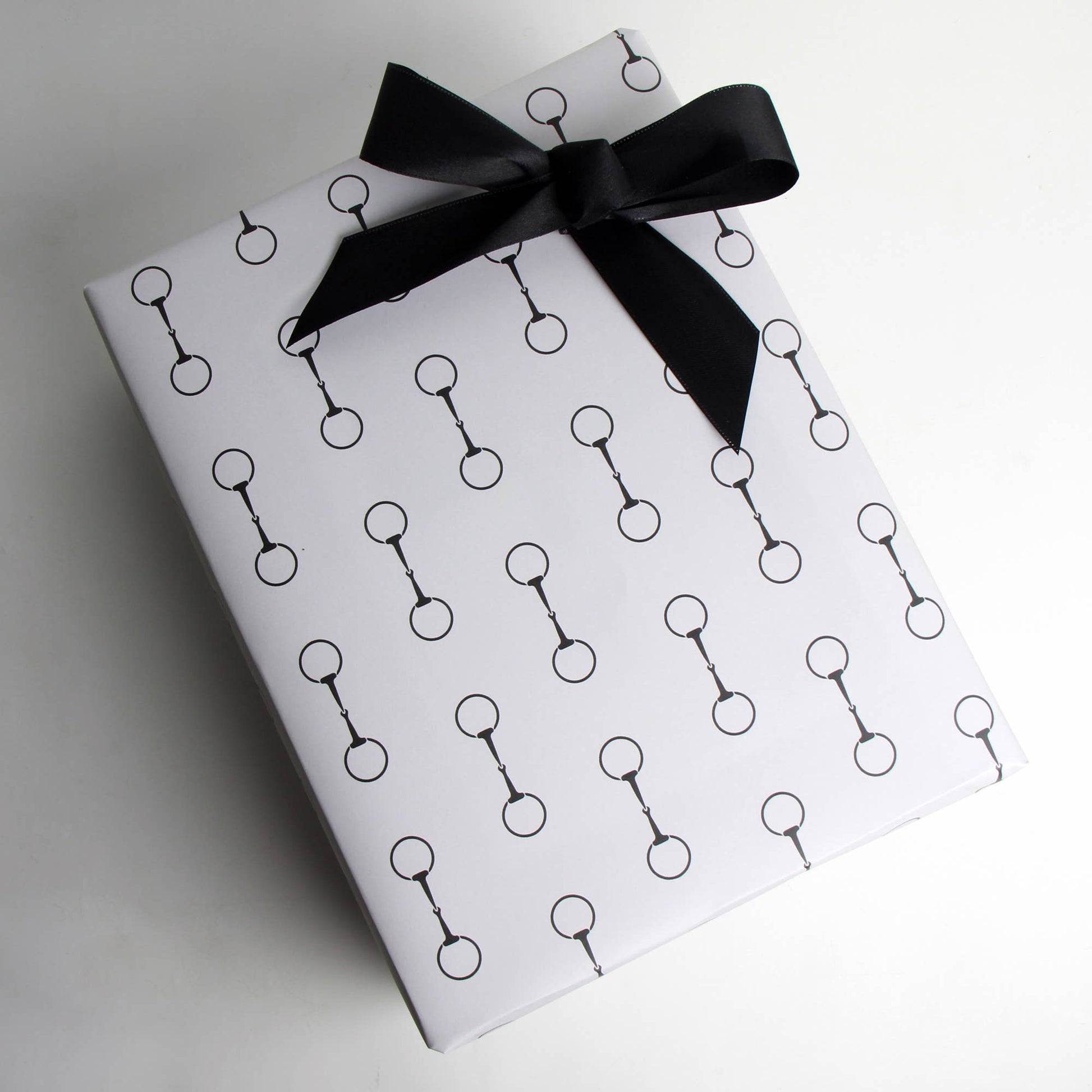Gift box wrapped in paper with black snaffle bit pattern and tied with a black ribbon on a white background