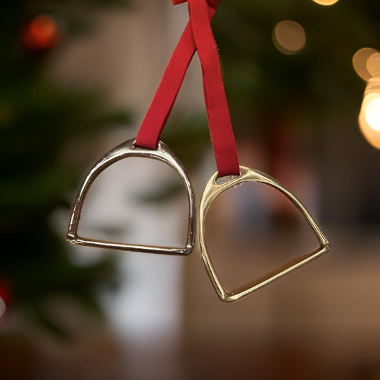 Two metal stirrups on red ribbons against a blurred Christmas tree background