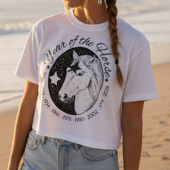Person wearing a white t-shirt with a horse graphic and text on a beach.
