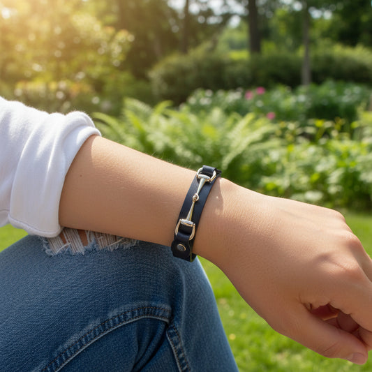 Person wearing a black leather bracelet with a gold horse bit on a blurred green outdoor background