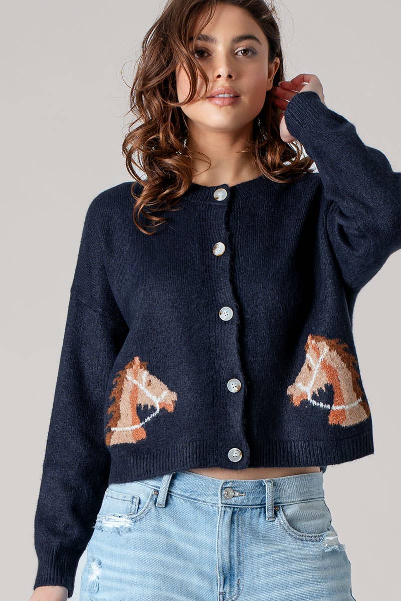 Woman wearing a navy blue cardigan with horse designs on a plain background