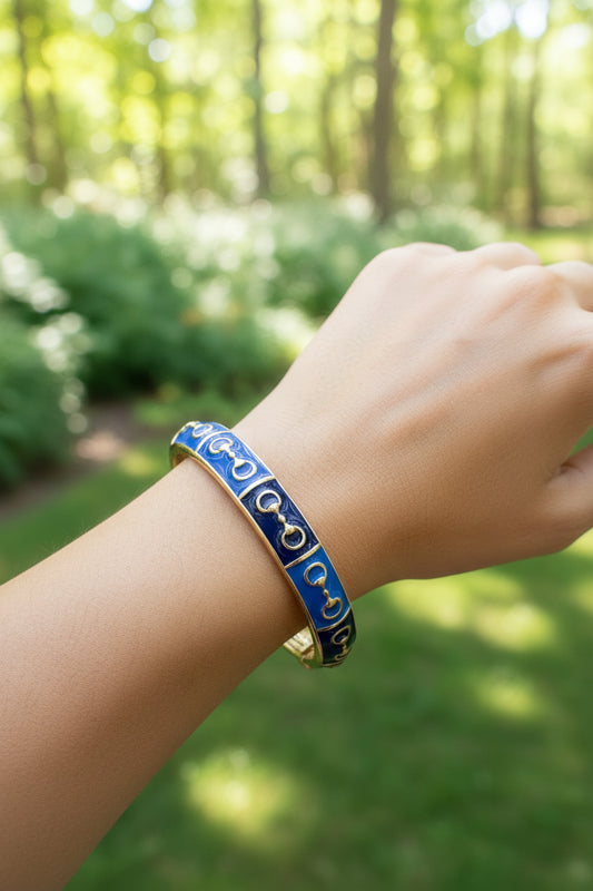 Hand wearing a blue and gold bracelet with a blurred forest background