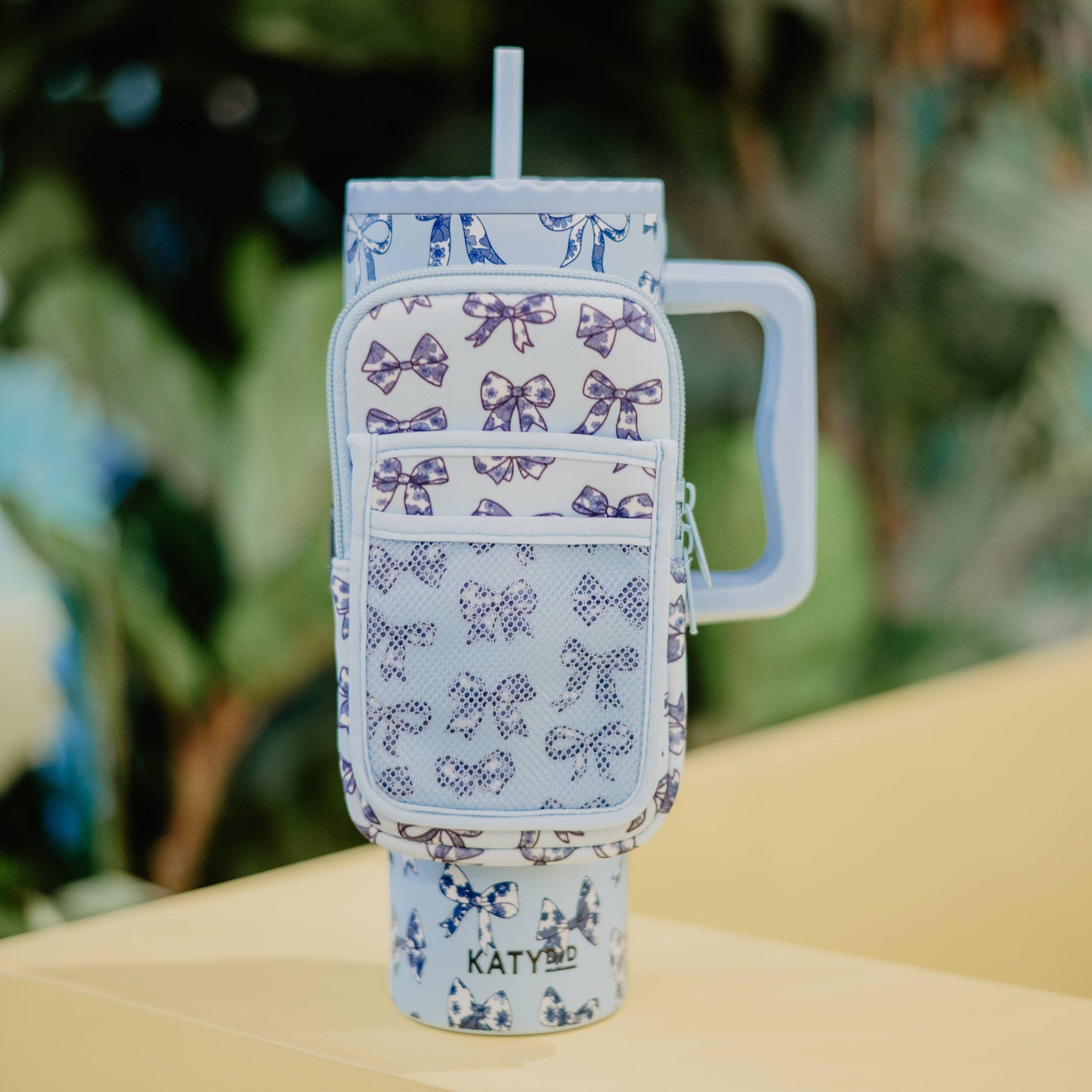 A neoprene pouch with floral bows design in blue color, attached to a tumbler, designed to hold cards or phones.