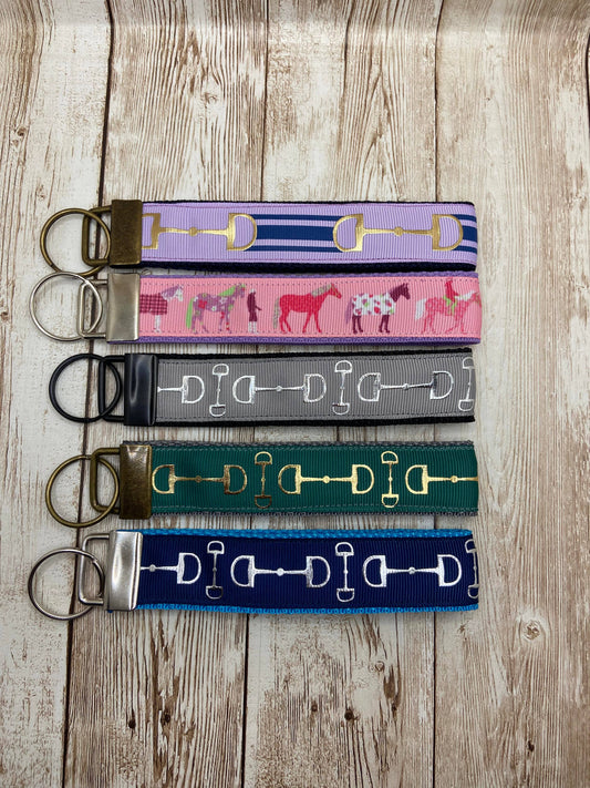 A collection of equestrian-themed webbed keychains with various patterns, displayed on a wooden background.