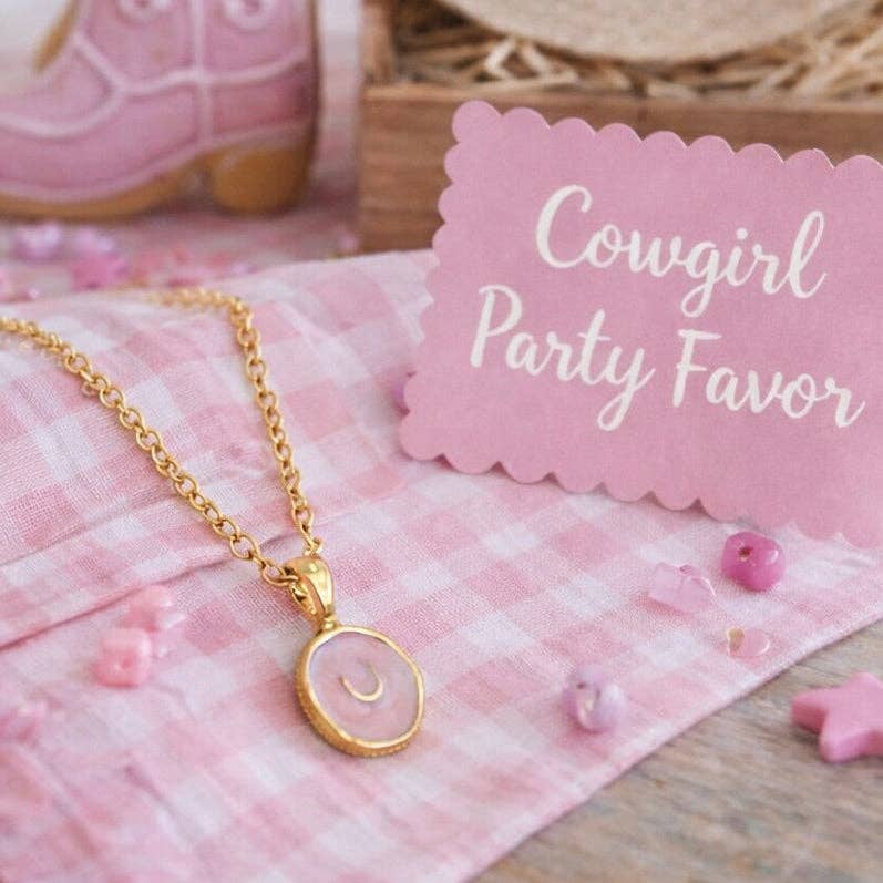 Gold necklace with pink pendant on a pink checkered cloth with 'Cowgirl Party Favor' sign.