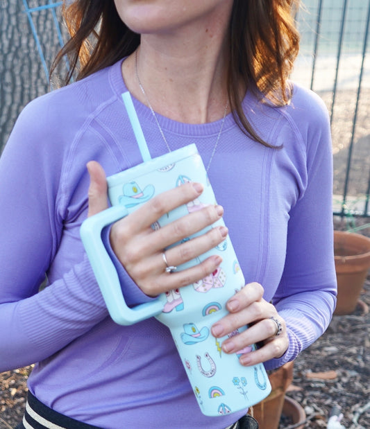 A person holding a mint blue colored tumbler with a cowgirl design and a straw.