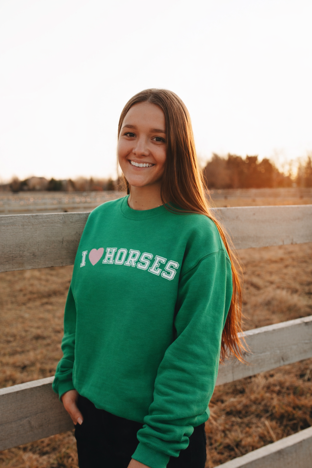 Person wearing a green sweatshirt with 'I ❤️ HORSES' text, standing in an open field.