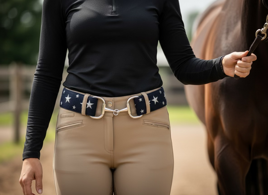 Person wearing a black long-sleeve top and beige riding pants with a star-patterned riding belt, standing next to a horse.