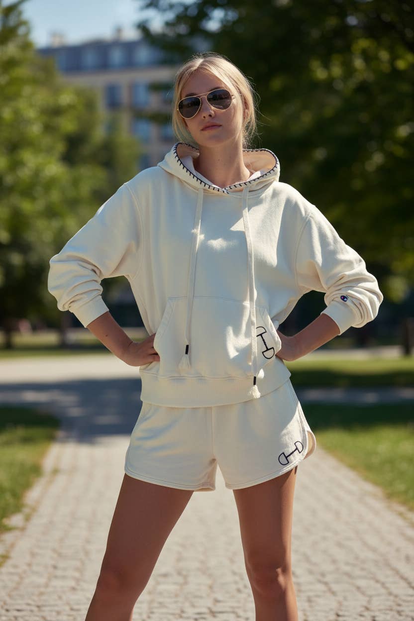 Person wearing a white hoodie and shorts  lounge wear set with sunglasses outdoors.