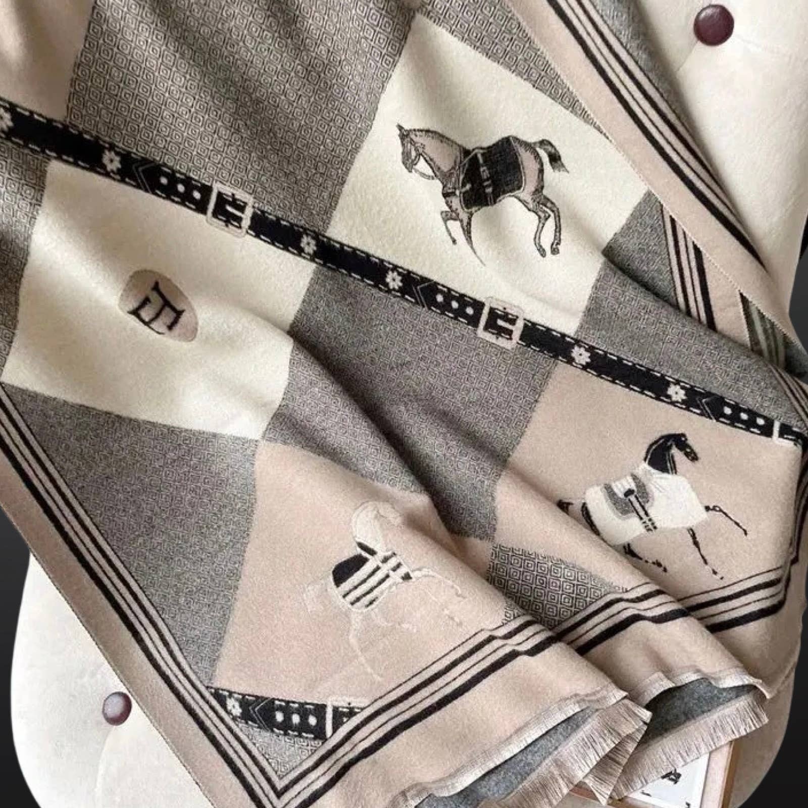 Close-up of an equestrian winter scarf with a geometric pattern featuring horses and riding bits, predominantly in beige, black, and gray tones.