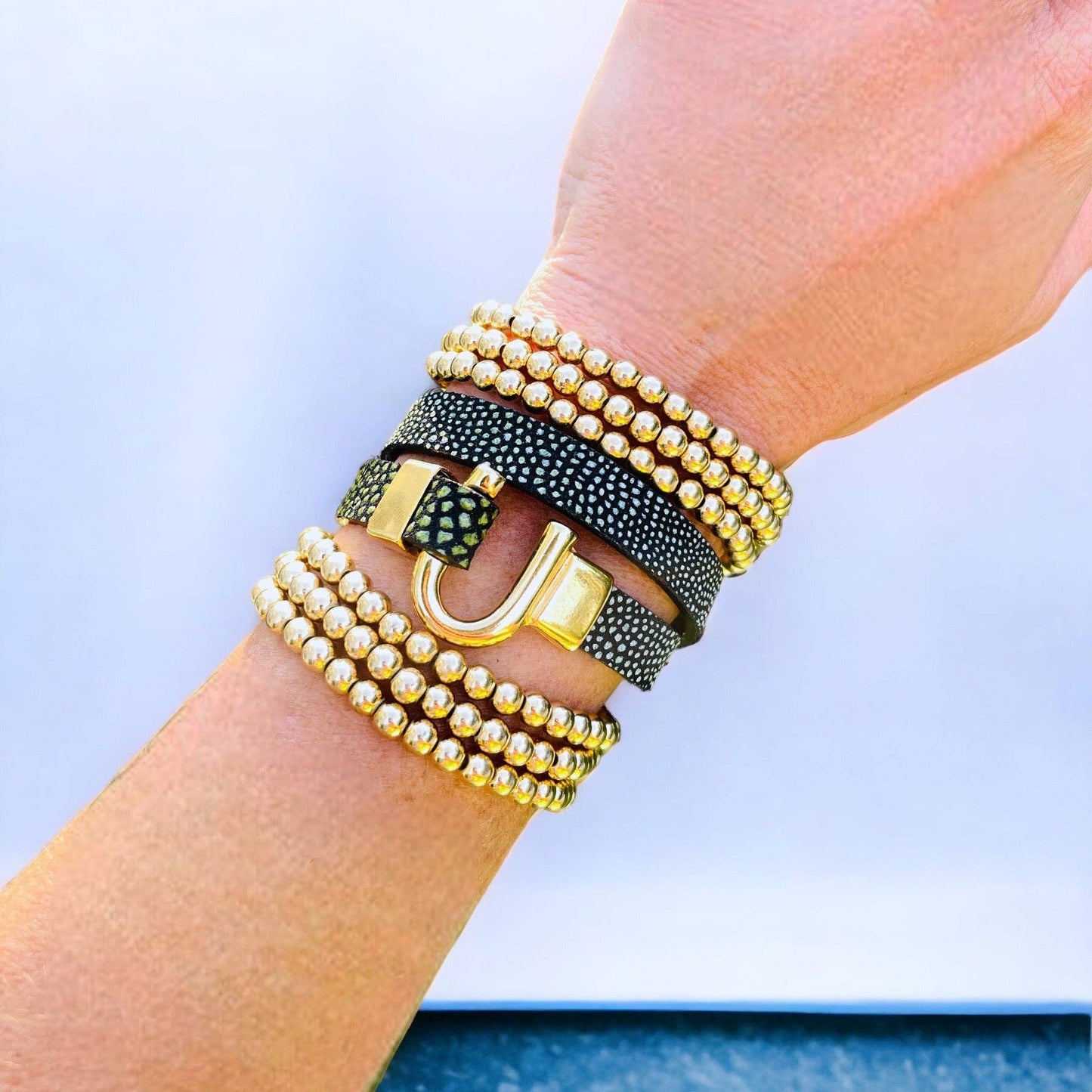 A person's wrist wearing a black and gold horseshoe leather bracelet wrap with a textured pattern.