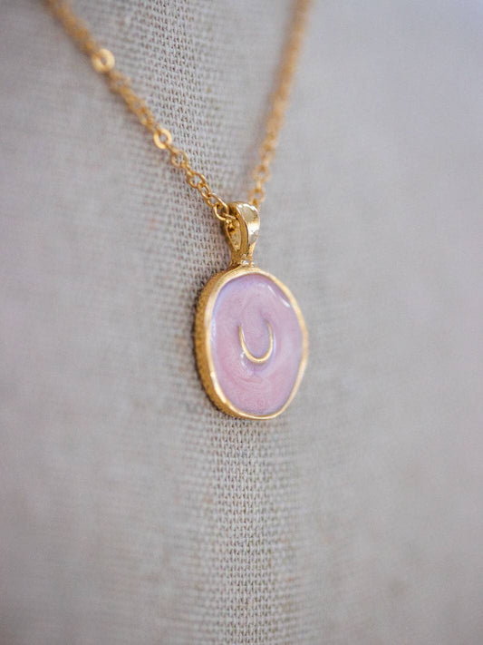 Necklace with a pink pendant with a gold horse show and gold chain on a gray fabric background