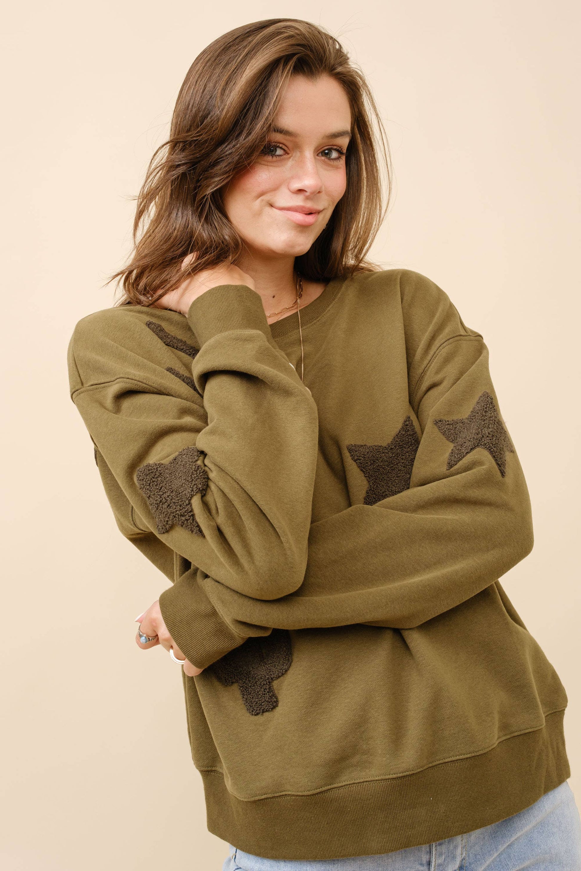 A woman wearing a green textured patchwork sweatshirt with star and cactus designs.