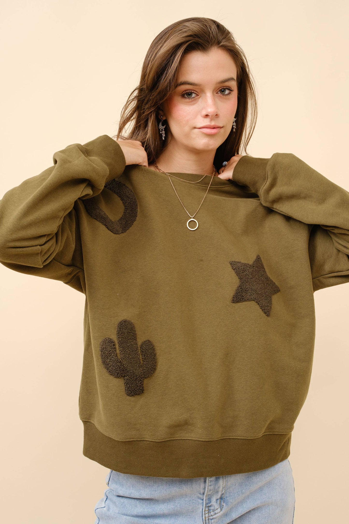 A woman wearing a green textured patchwork sweatshirt with star and cactus designs.