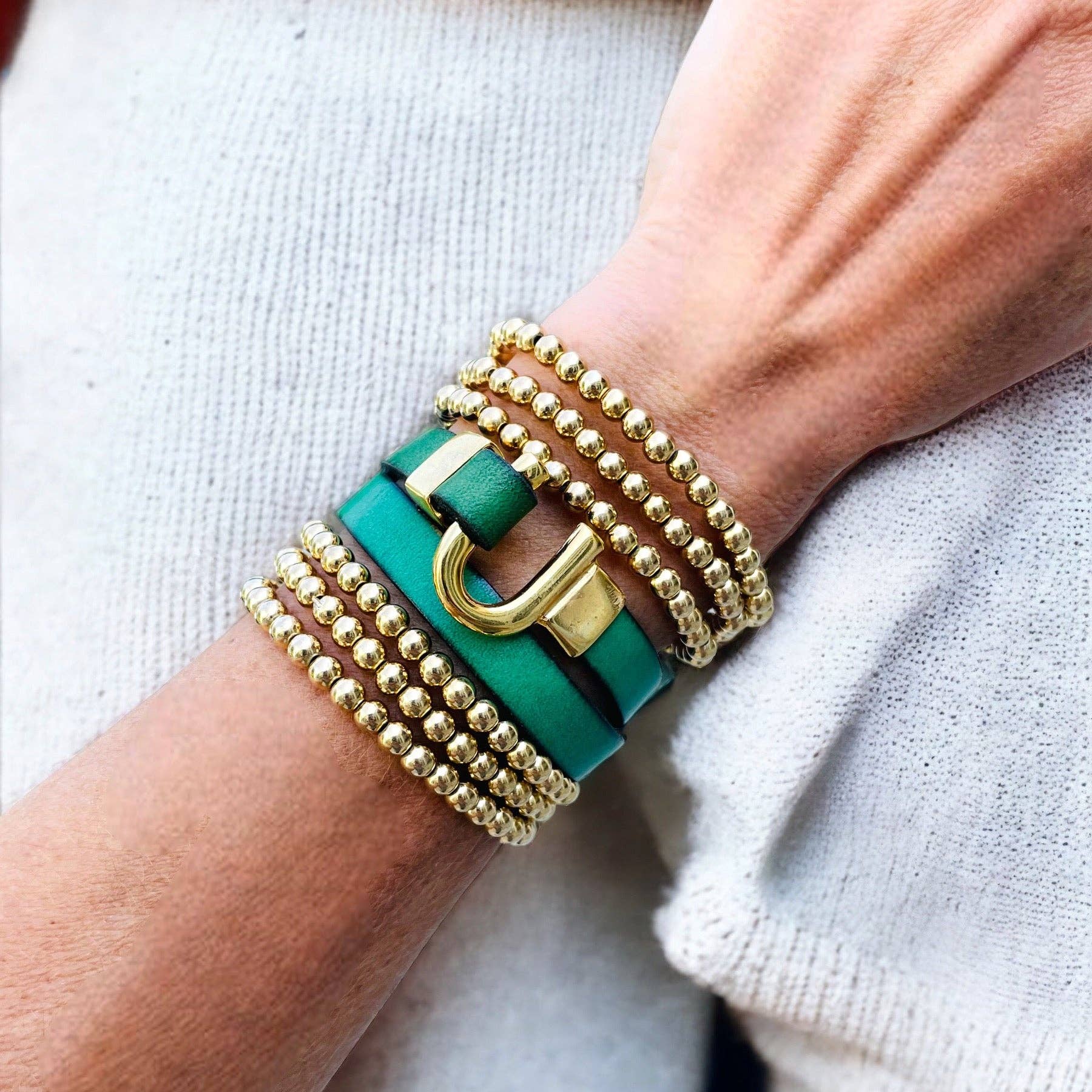 green leather bracelet wrap with a horse shoe closure, and a gold beaded bracelet stack