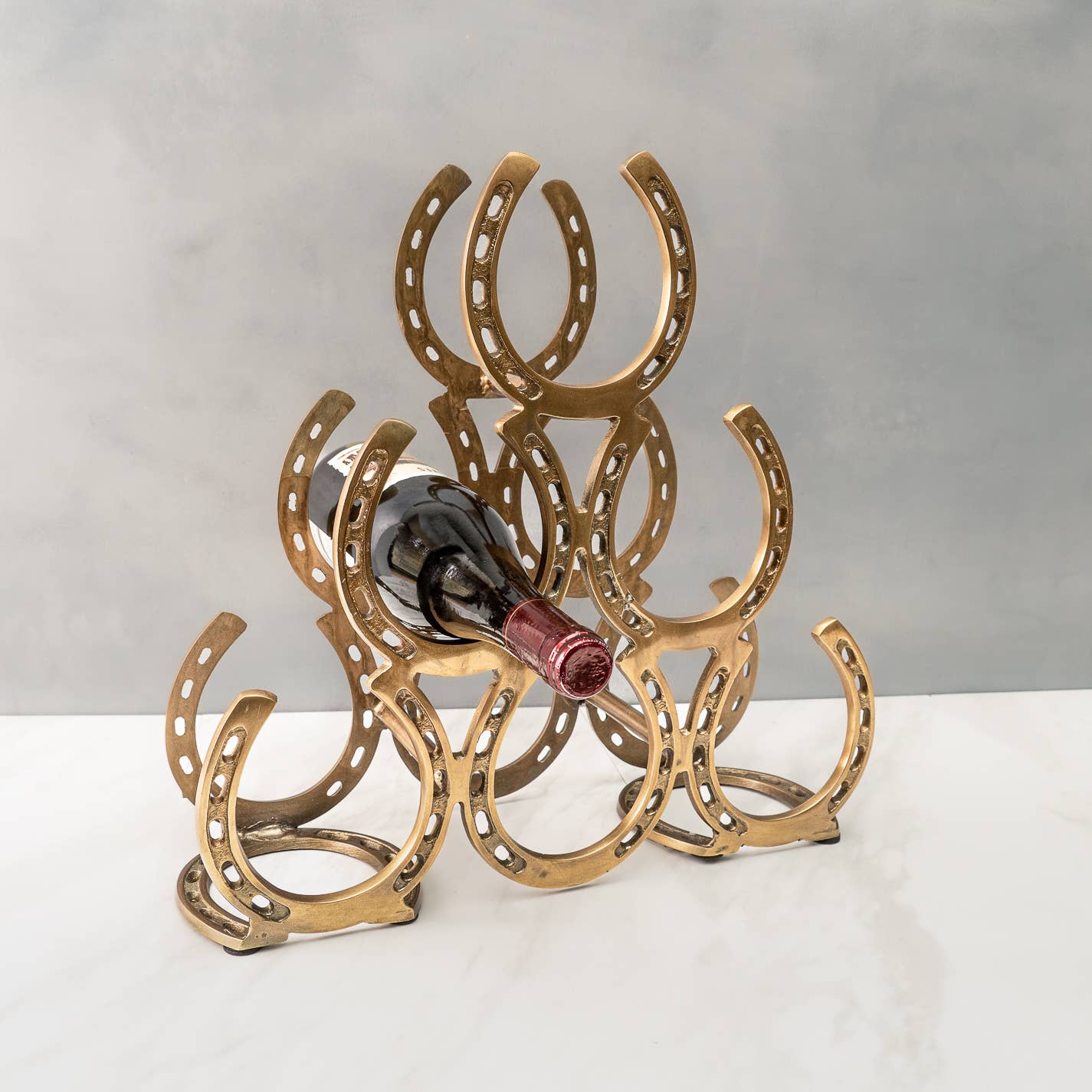 A chrome aluminum 6-bottle wine rack in the shape of a horseshoe, with the rack holding six wine bottles, placed on a marble surface.
