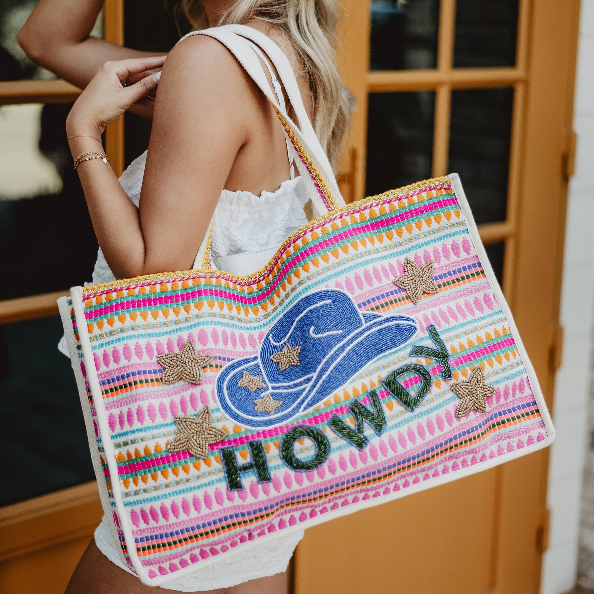 A person carrying a multicolored striped tote bag with a cowgirl hat graphic and the text 'HOWDY' on it.