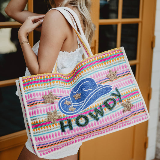 A person carrying a multicolored striped tote bag with a cowgirl hat graphic and the text 'HOWDY' on it.