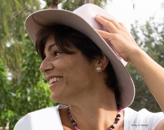 woman smiling wearing a hat and sterling silver earrings of a jumping horse