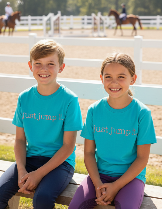 Two children wearing 'just jump it' t-shirts sitting on a wooden bench with equestrian background.