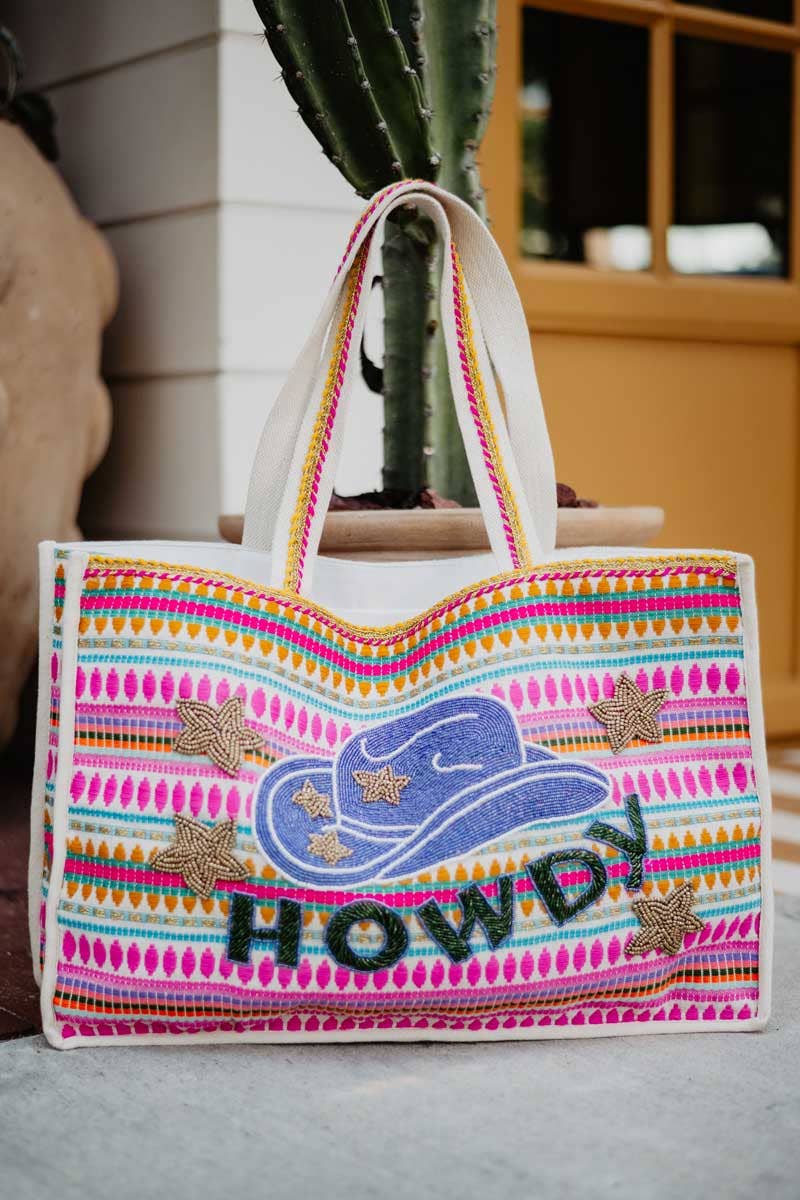 A person carrying a multicolored striped tote bag with a cowgirl hat graphic and the text 'HOWDY' on it.