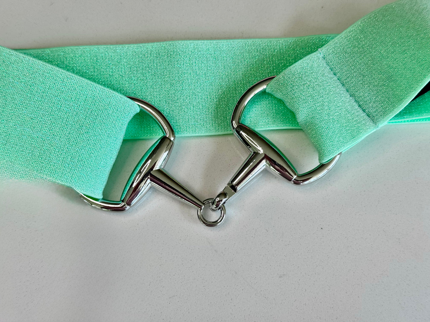 A collection of three sparkle bit belts in silver, purple, and blue colors with chrome hardware and a snaffle bit buckle closure.