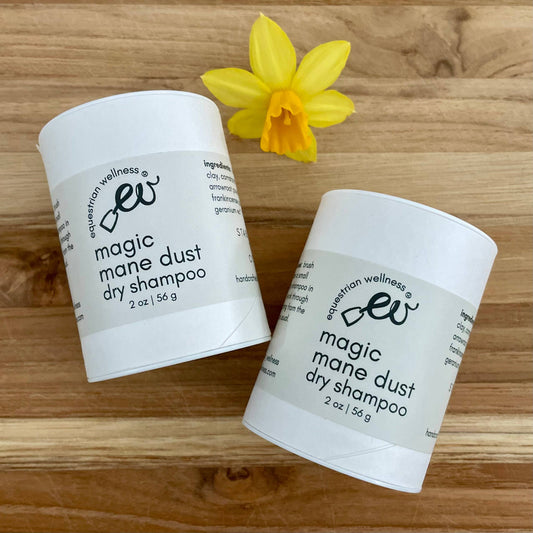 Two containers of 'Magic Dry Shampoo' by Equestrian Wellness, with a decorative yellow flower beside them, on a wooden surface.